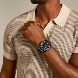 Man wearing a Fossil Machine watch with a black stainless steel band, styled with a casual beige polo shirt